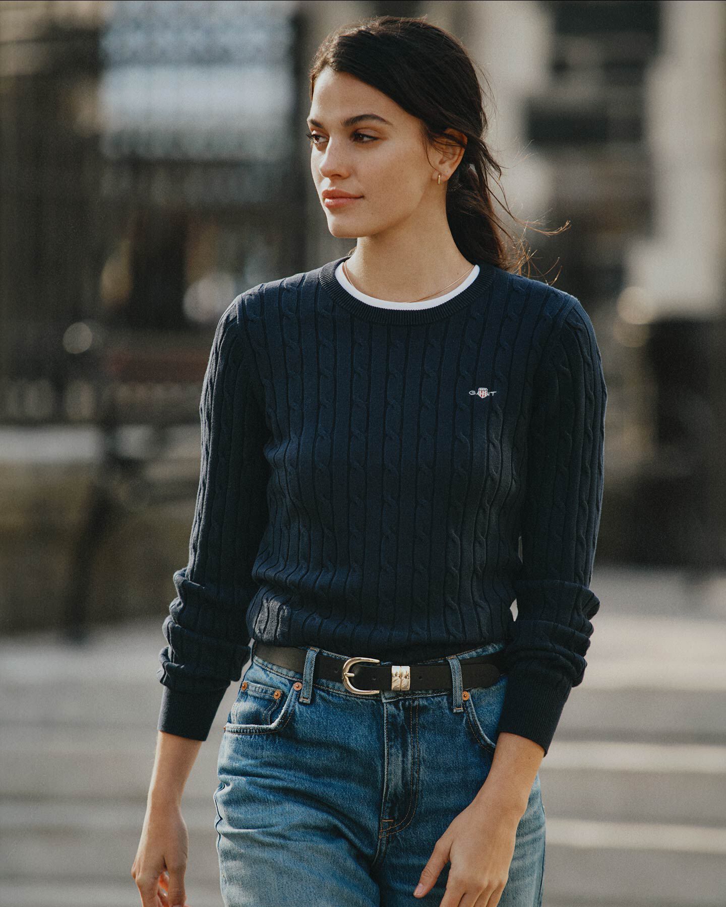 Woman walking outdoors wearing a Gant navy cable-knit sweater.